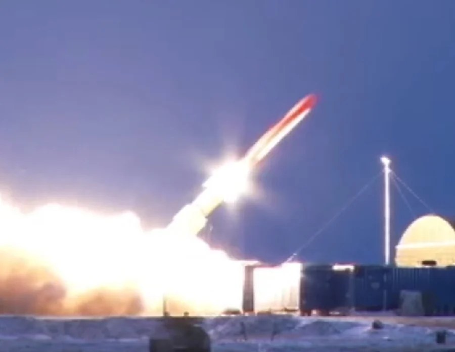 Dusk ground launch of a missile with a bright exhaust flame beside a dome and shipping containers on snowy ground; the date and place are not stated in the source and are not confirmed