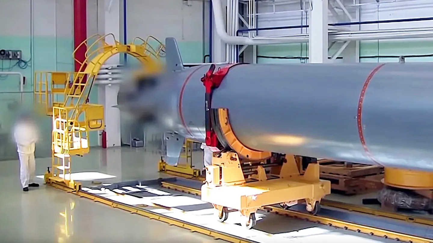 Poseidon torpedo body in a factory assembly hall, with a worker and yellow handling gantry (Russian MoD footage frame)