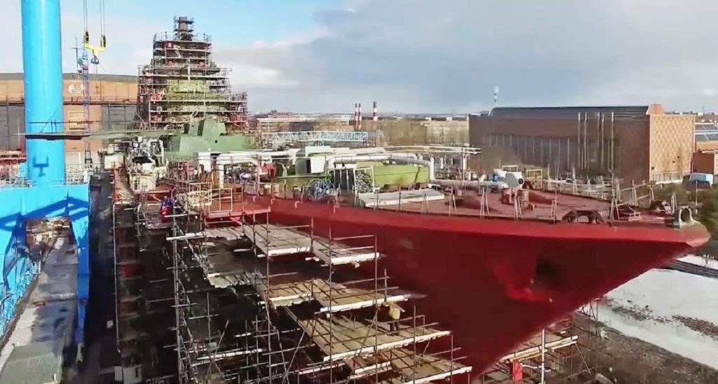 Heavy cruiser hull painted red with scaffolding in a shipyard, superstructure under construction