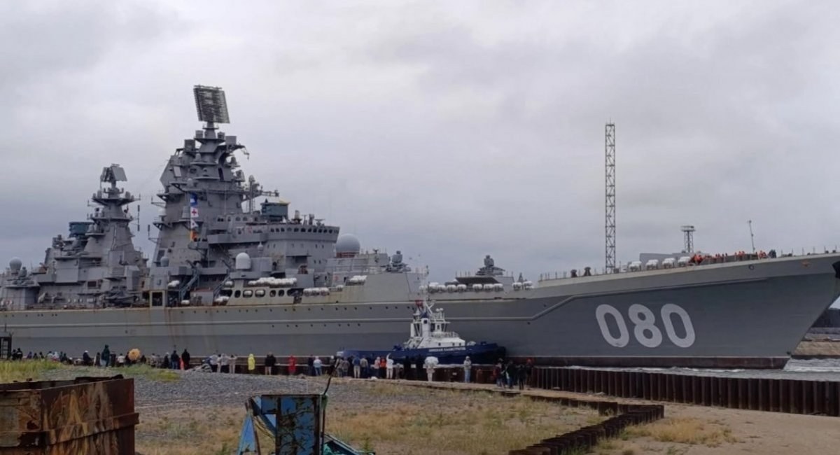 Kirov-class cruiser with hull number 080 moving past a quay with a tug and spectators